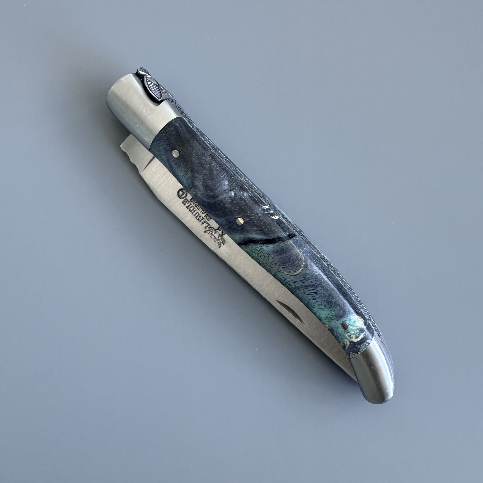 Closed Laguiole en Aubrac folding knife showing the full blue-green elder burl handle and brand markings on the blade spine