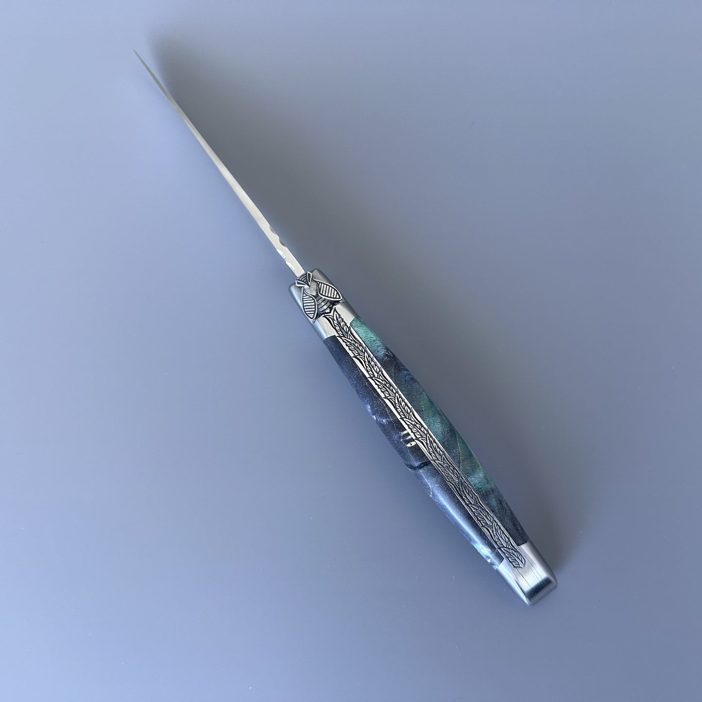 Open Laguiole en Aubrac pocket knife with elder burl handle and etched steel blade, shown blade-right with visible maker's mark