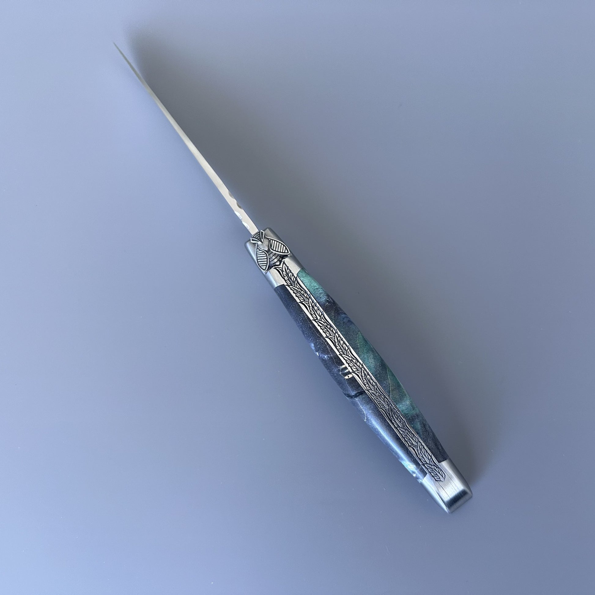 Open Laguiole en Aubrac pocket knife with elder burl handle and etched steel blade, shown blade-right with visible maker's mark
