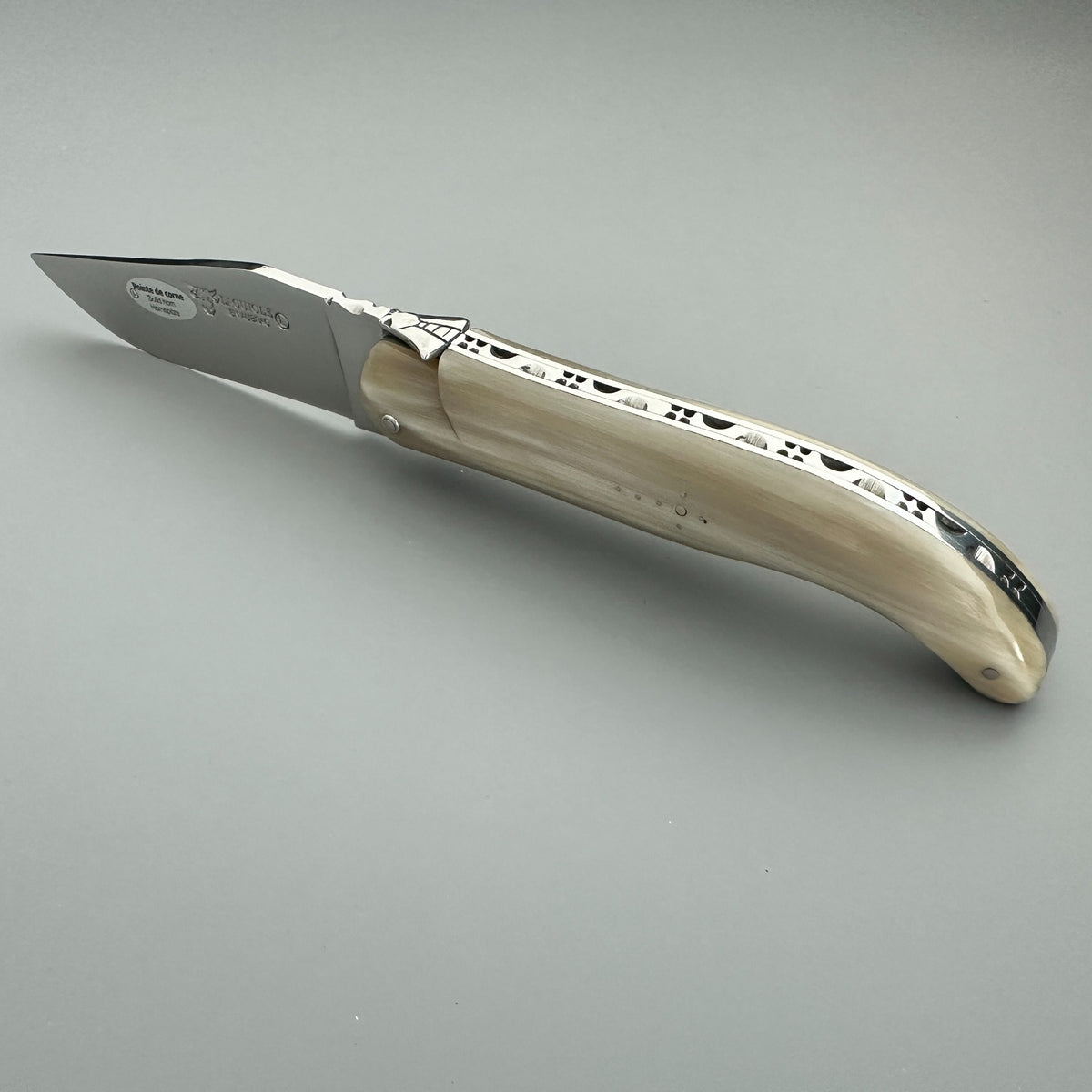 Laguiole en Aubrac Hunting Knife with a silver stainless steel blade and a cream-colored bone handle featuring black engraved patterns, shown on a neutral gray background.