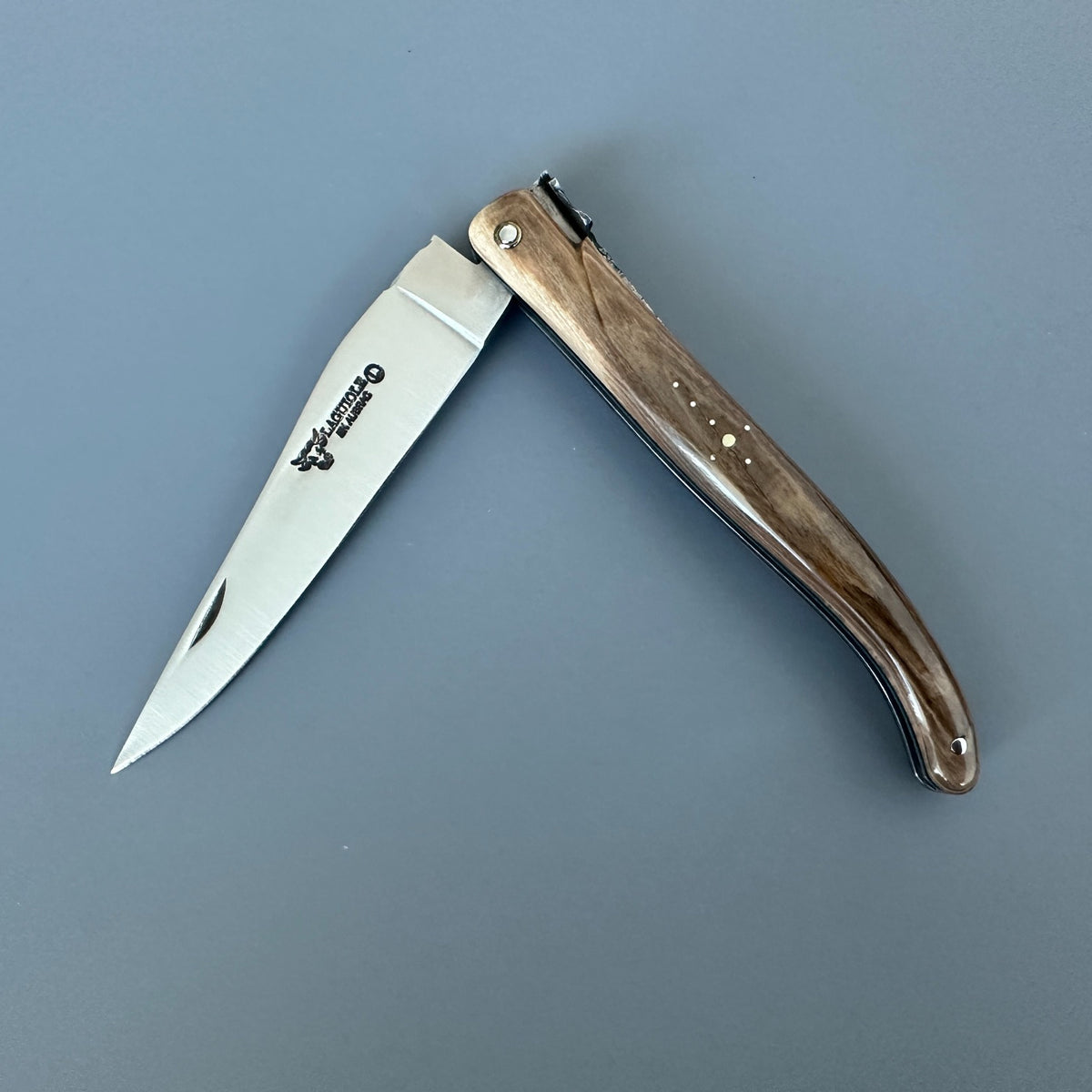 Laguiole en Aubrac mammoth ivory folding knife partially open, showing the blade logo and decorative handle pins
