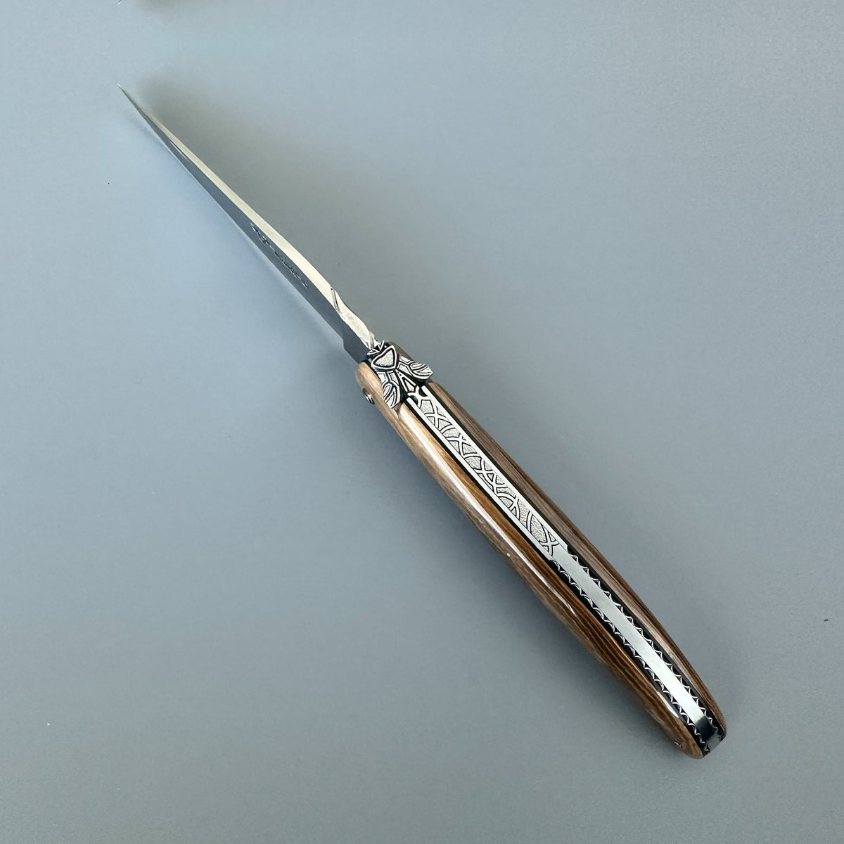 Cenital view of the open Laguiole en Aubrac mammoth ivory folding knife, highlighting the handle and engraved spine