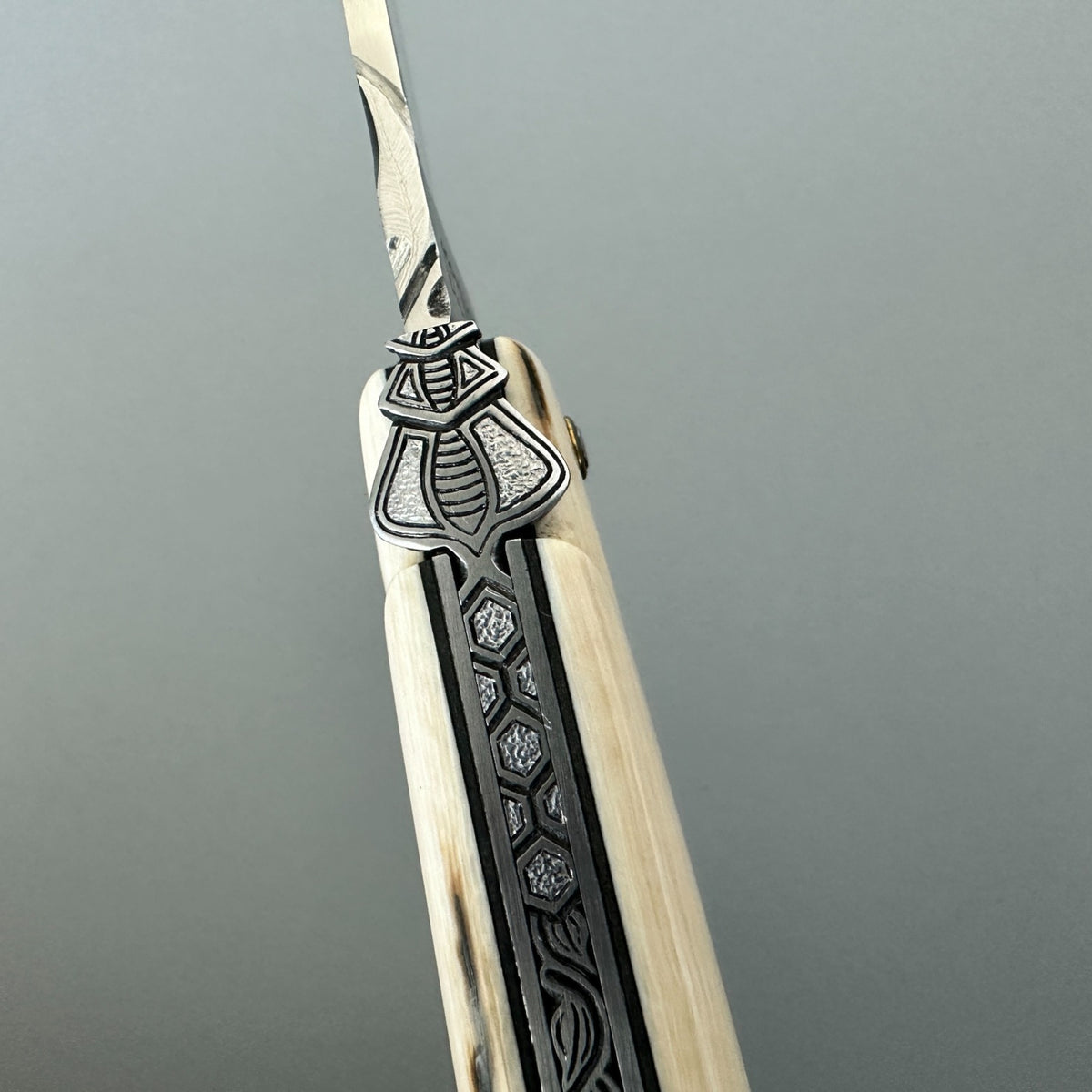 Close-up of the engraved bee and decorated spring between the mammoth ivory handle scales of a Laguiole en Aubrac knife.