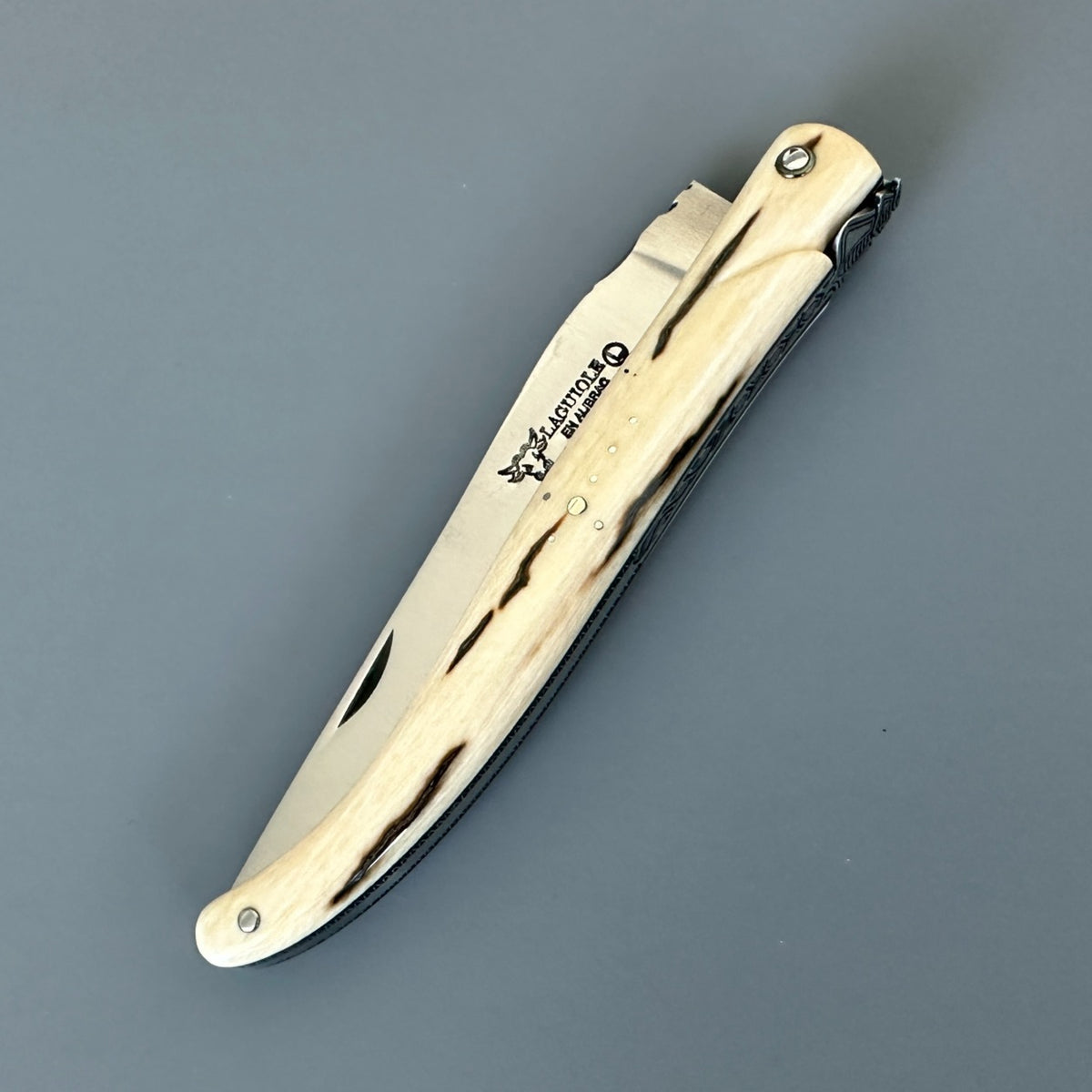 Closed Laguiole en Aubrac folding knife with a cream mammoth ivory handle featuring dark streaks.