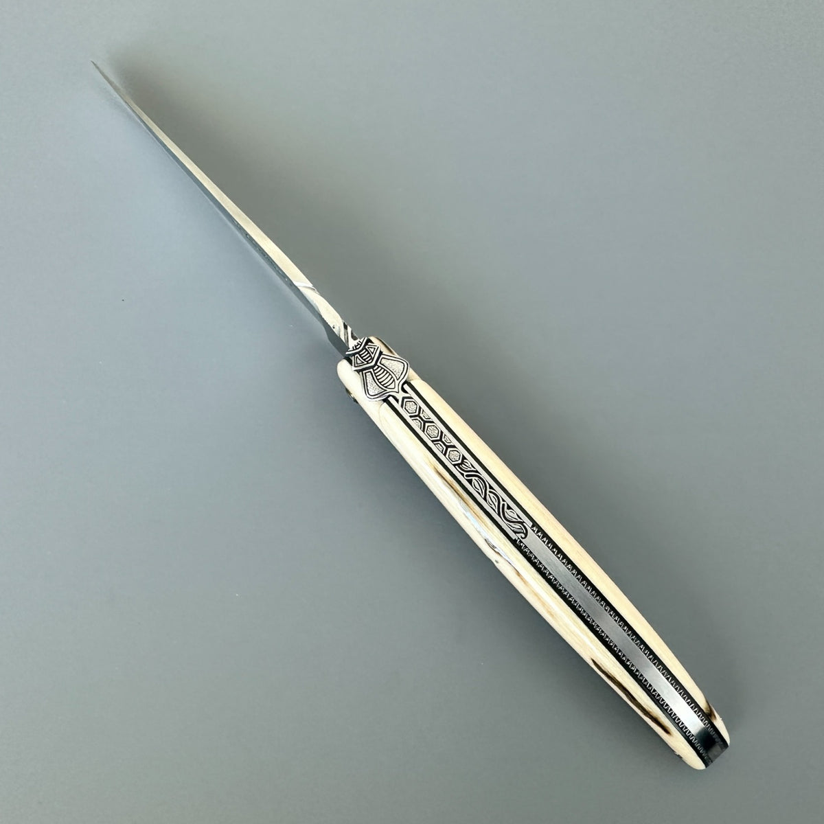 Laguiole en Aubrac mammoth ivory folding knife viewed from above, showing the decorated spine and open blade.