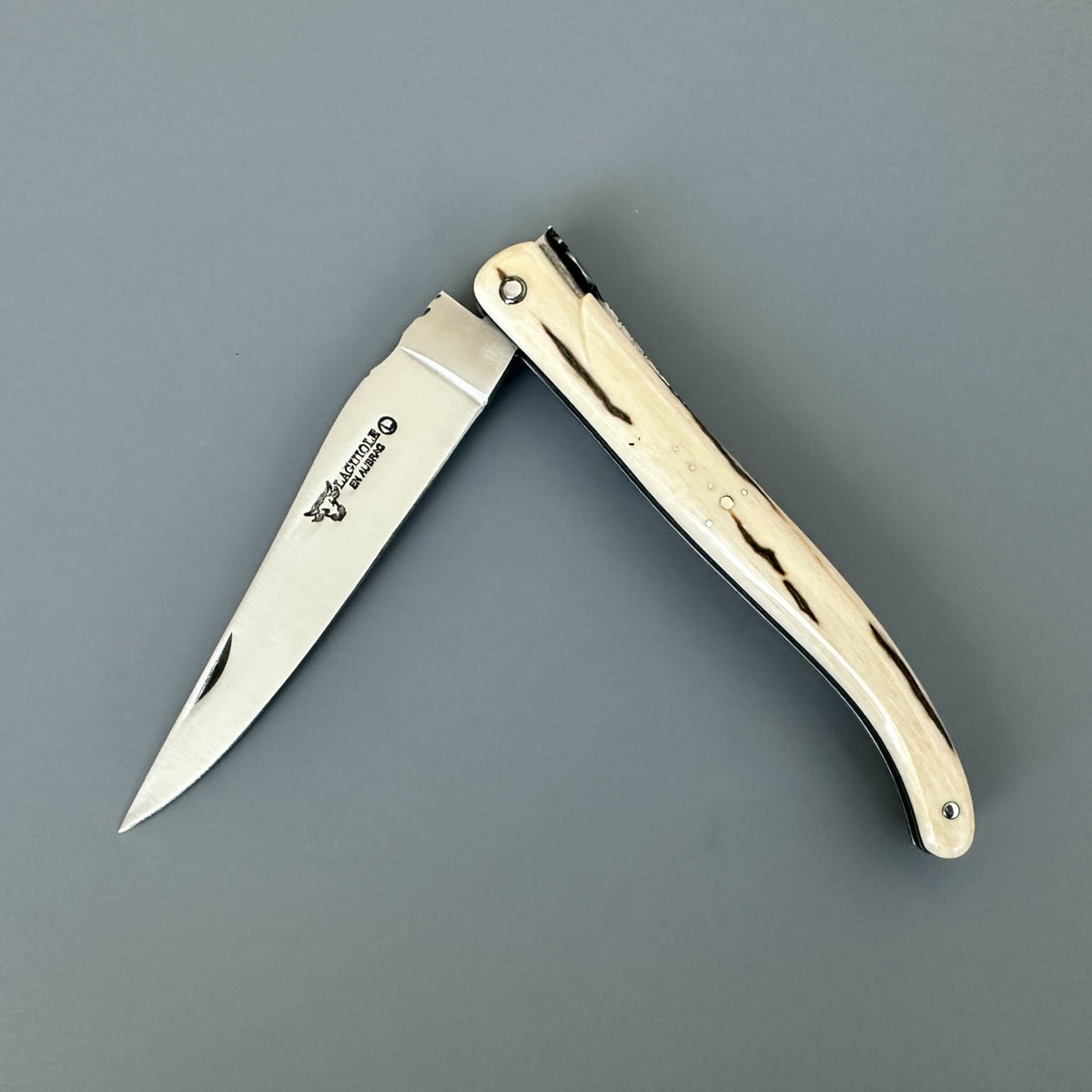 Partially open Laguiole en Aubrac folding knife with streaked mammoth ivory handle and blade logo.
