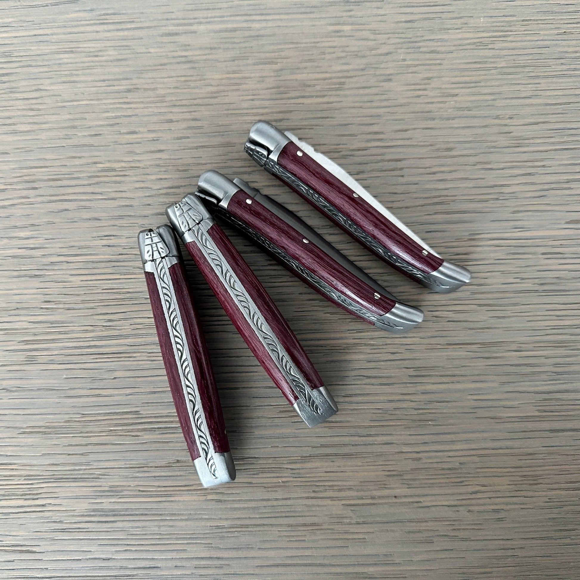 Four Laguiole en Aubrac Mini Folding Knives with Amaranth handles arranged to show their sides and decorated spines.