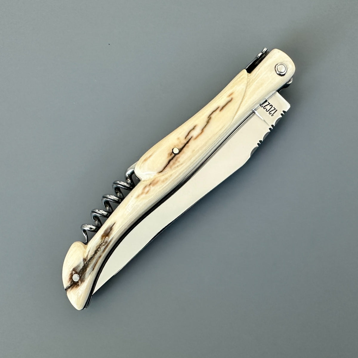 Reverse side of a closed Laguiole en Aubrac folding knife with a streaked pale handle and corkscrew.
