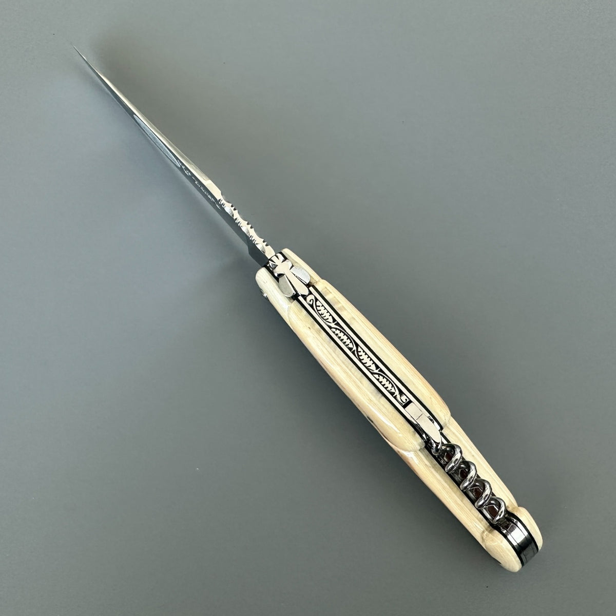 Top view of an open Laguiole en Aubrac folding knife showing the decorated spring, sculpted bee, and folded corkscrew.