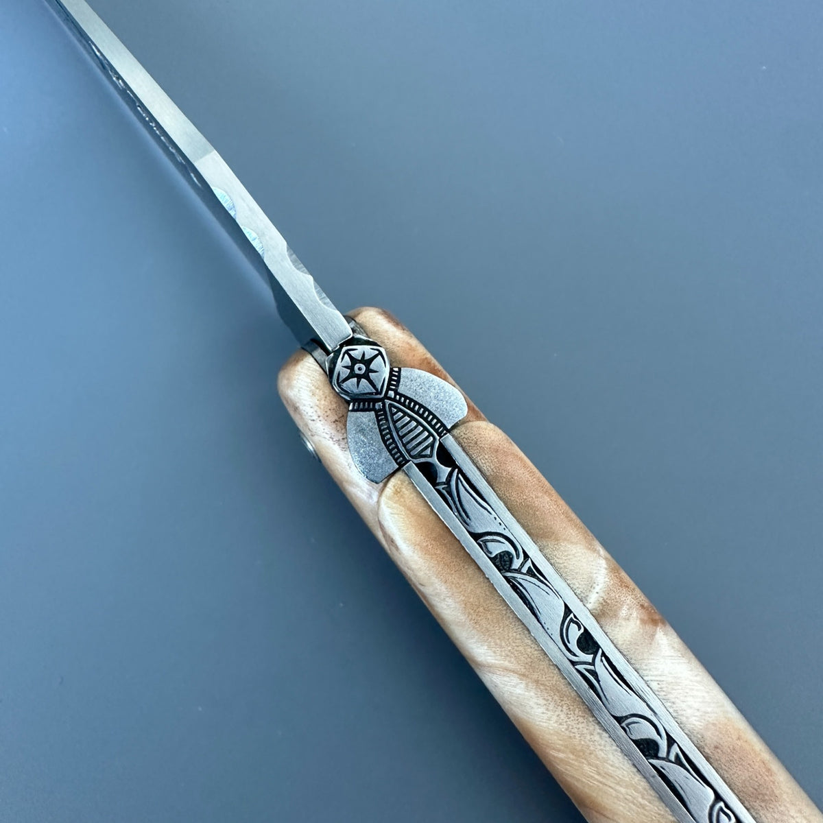 Close-up of the sculpted bee and engraved spring between the poplar handle scales of a Laguiole en Aubrac knife.