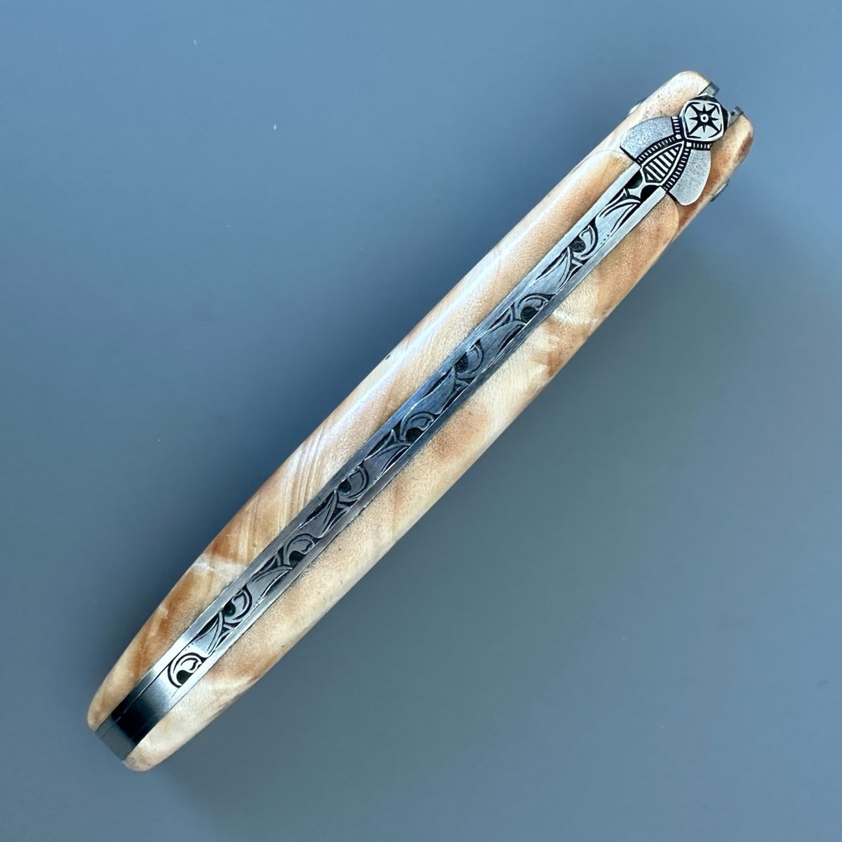 Closed Laguiole en Aubrac folding knife showing the golden poplar burl handle, decorative pins, and blade logo.