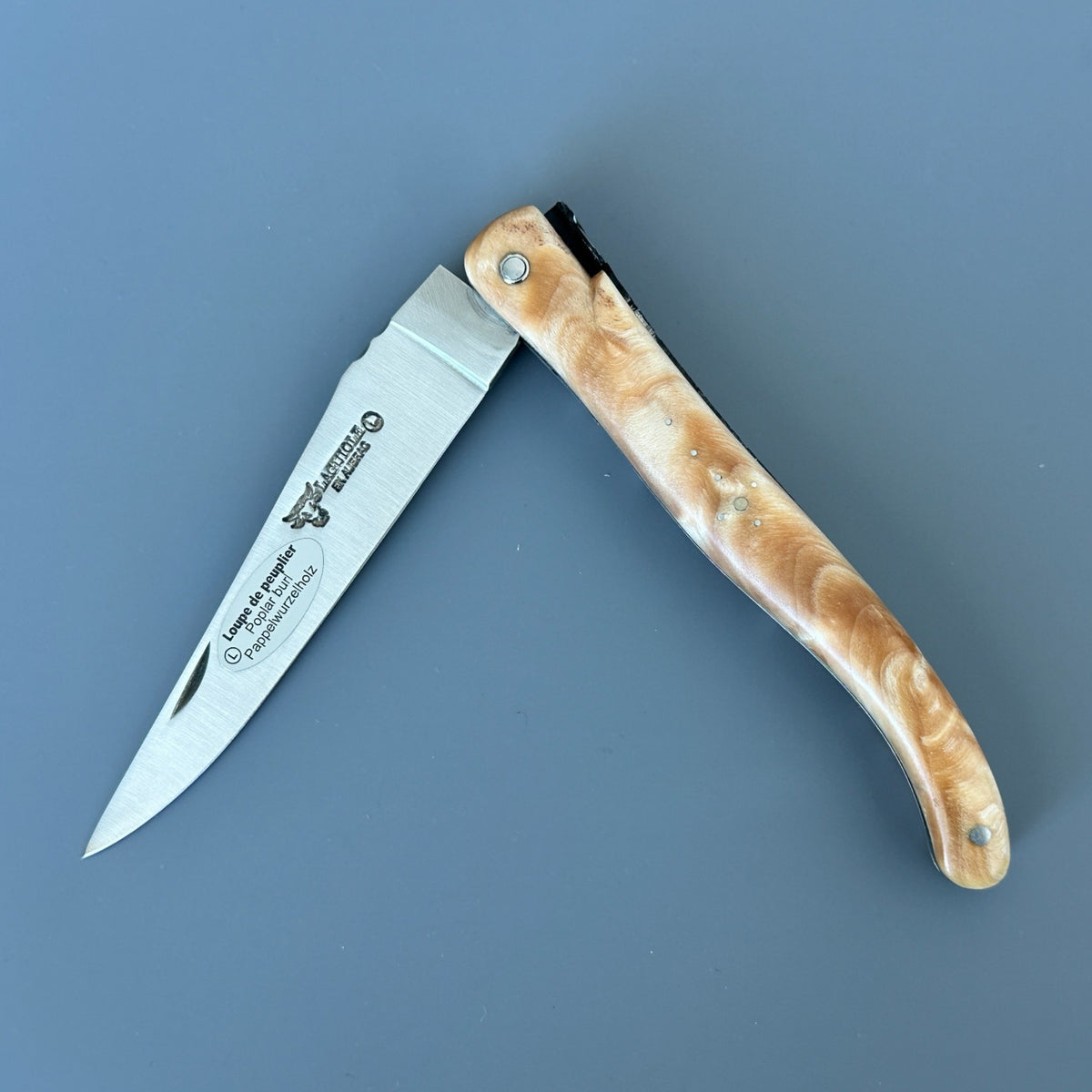 Partially open Laguiole en Aubrac folding knife with a golden poplar burl handle and blade logo.