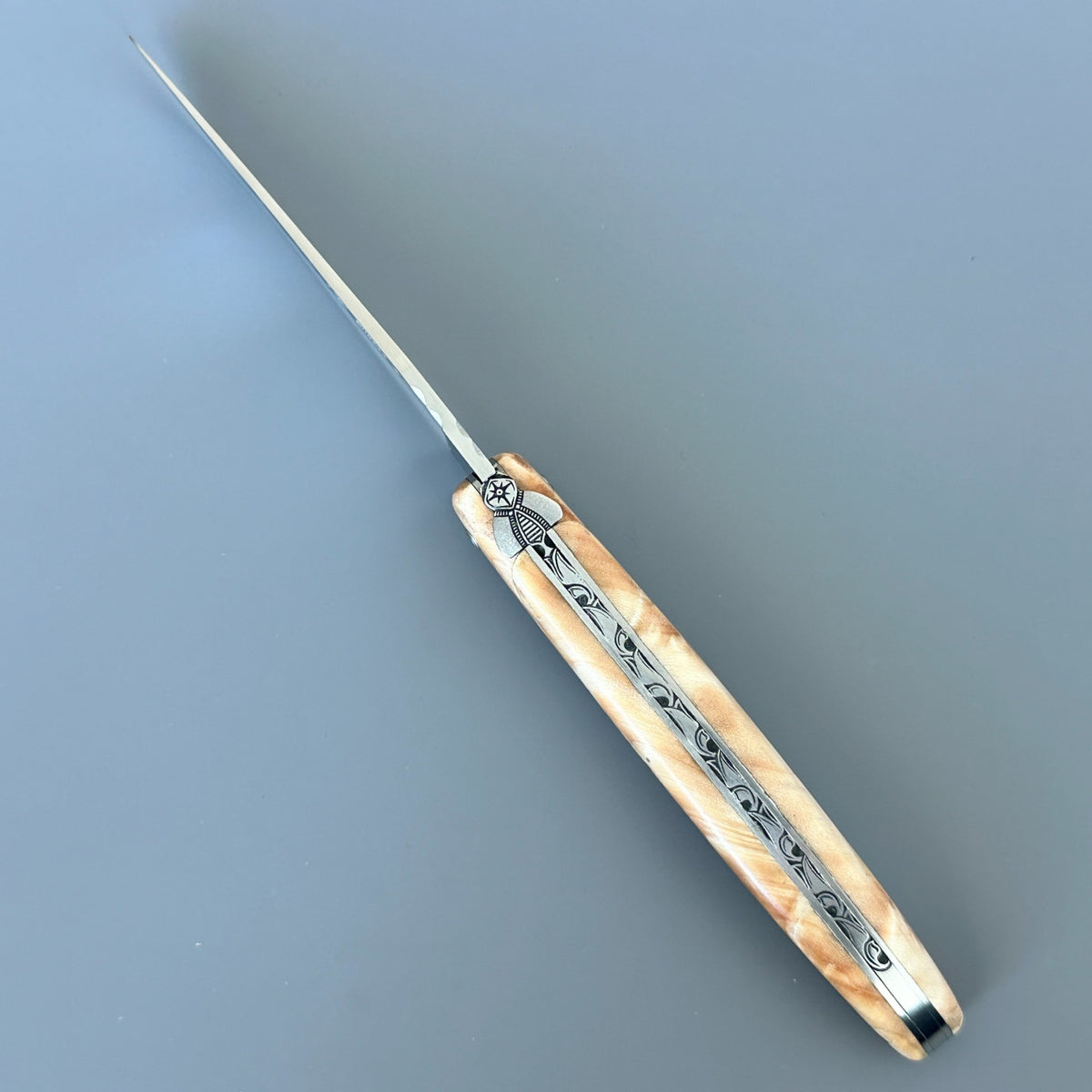 Top view of an open Laguiole en Aubrac poplar folding knife showing the decorated spring and sculpted bee.