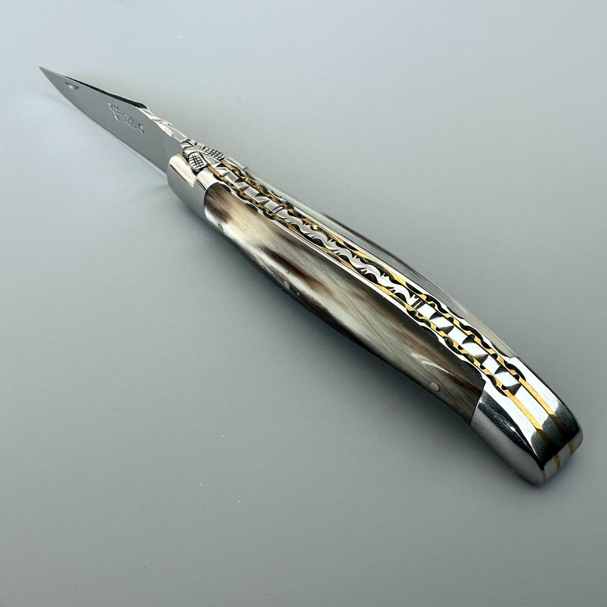 Beautiful Laguiole en Aubrac double-plated pocket knife with a solid horn handle, brass spine, in fully open position.