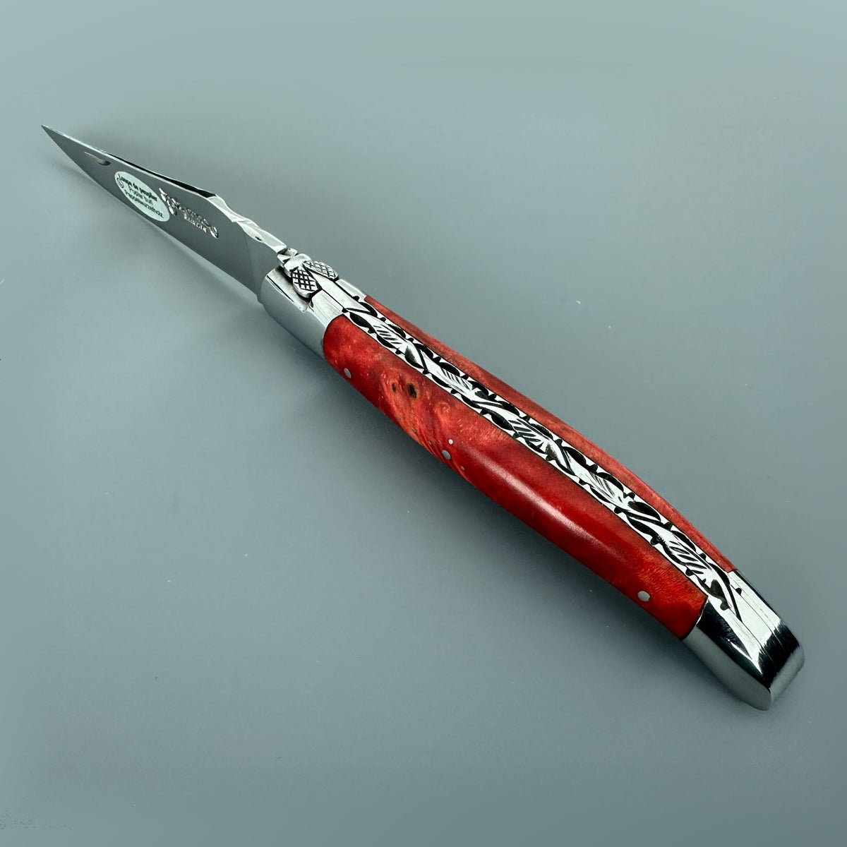 Open spine view of the Laguiole en Aubrac knife with a forged bee, hand-carved filework and stabilized red poplar handle.