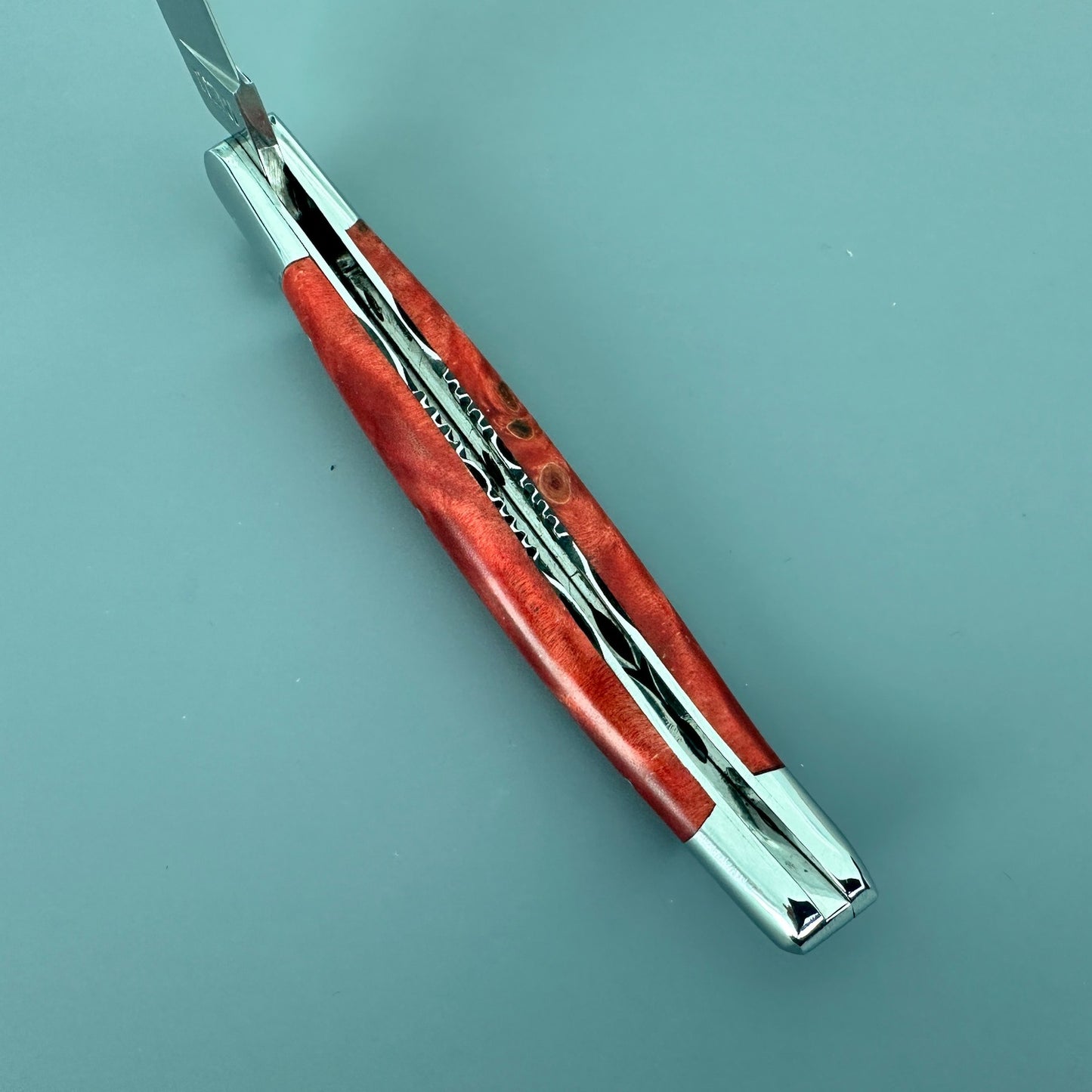 Blade and spine view of the Laguiole en Aubrac knife showing its stabilized red poplar handle and detailed metalwork.