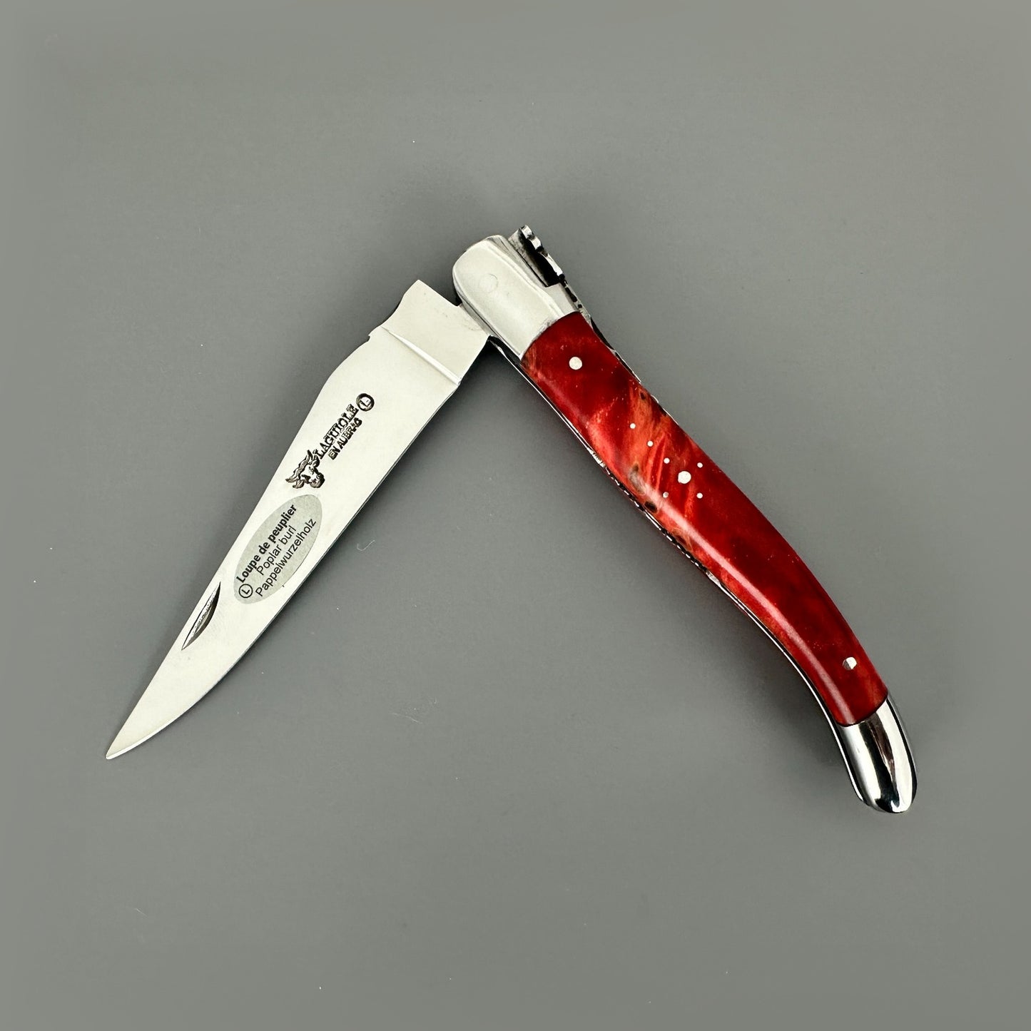 Open Laguiole en Aubrac knife with a stabilized red poplar handle, polished blade and hand-carved metalwork.