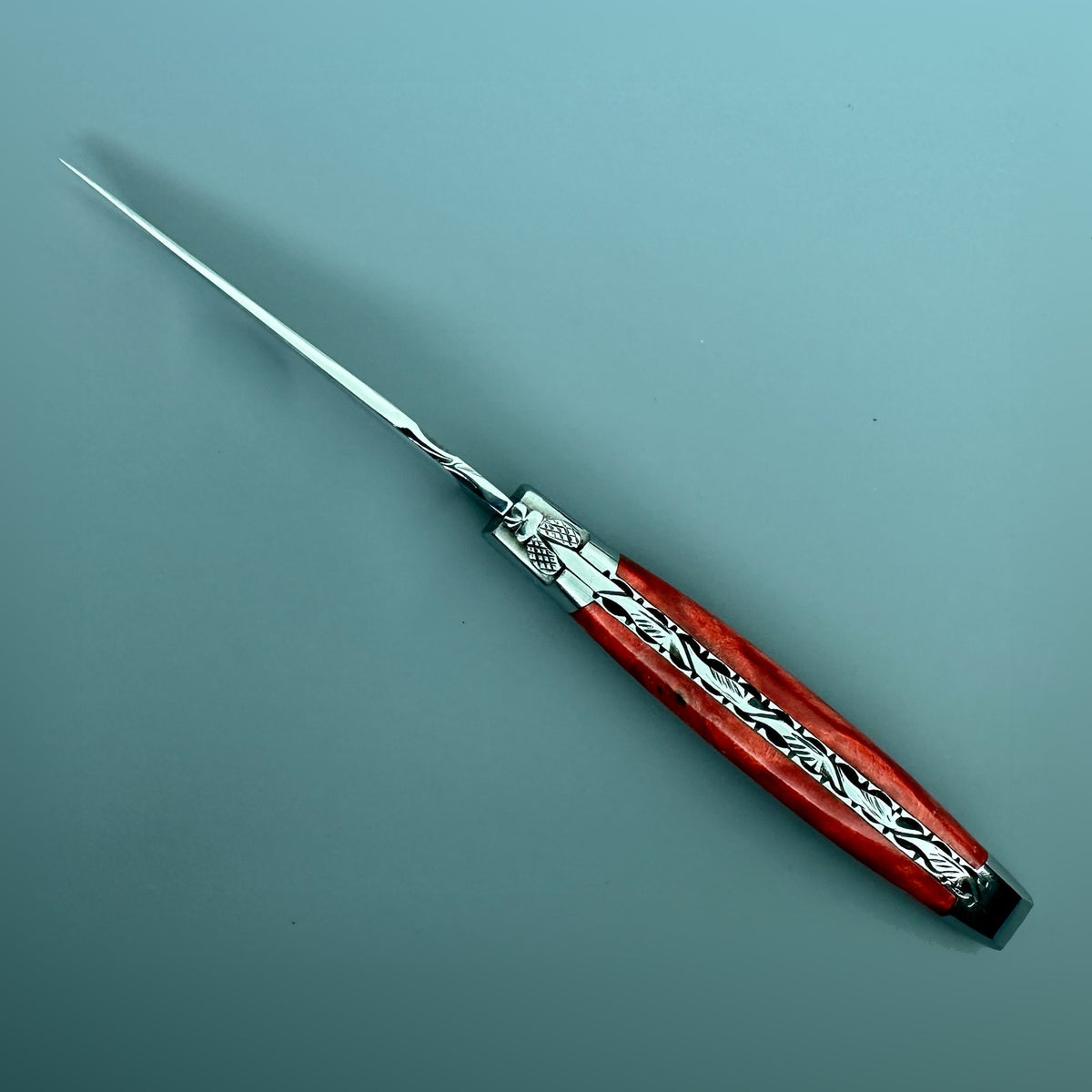 Angled view of the Laguiole en Aubrac stabilized red poplar knife highlighting its hand-carved spine and forged bee.