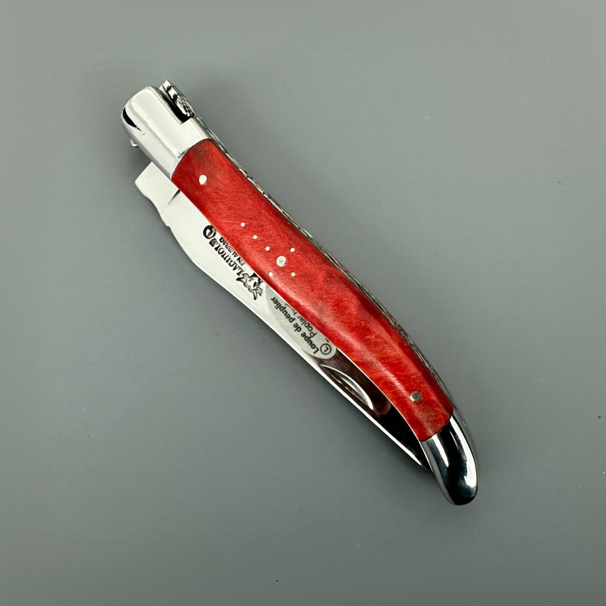 Closed Laguiole en Aubrac knife displaying its vivid stabilized red poplar handle and polished bolsters.